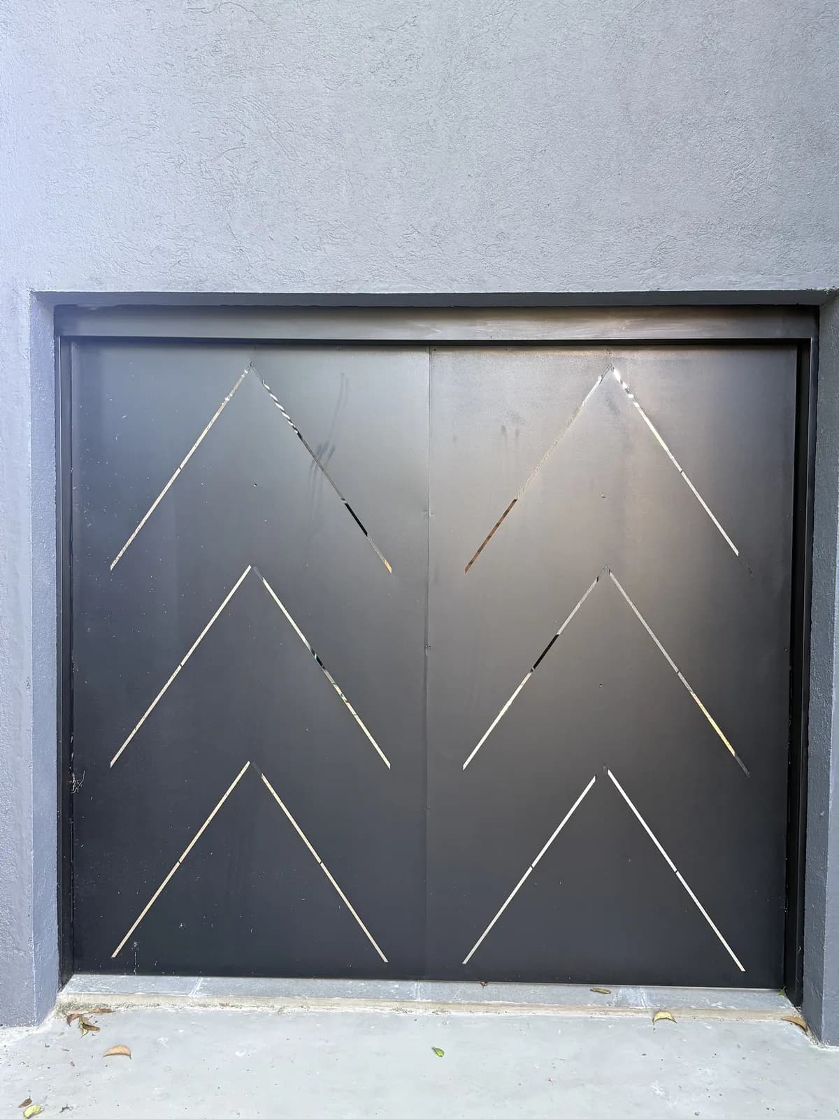 Puerta pivotante doble de chapa negra con diseño chevron calado, instalada